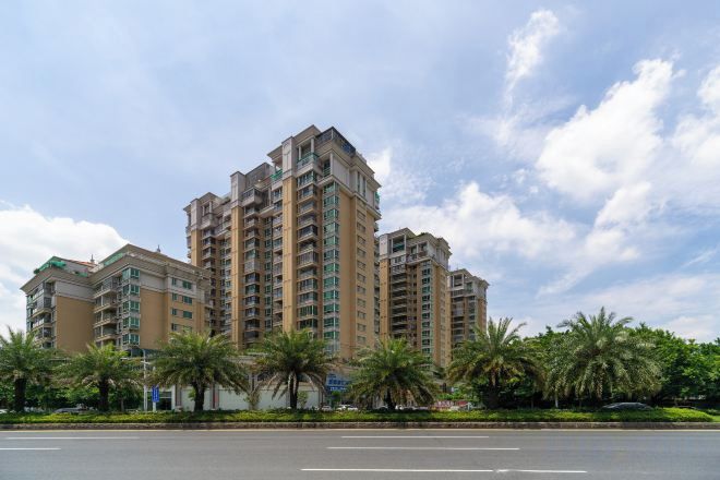 A multi-story residential building with a flat roof, surrounded by palm trees and a clear sky.