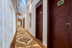 Ein Hotelgang mit einem aufwendigen Teppich, Holztüren und einer Deckenmalerei.