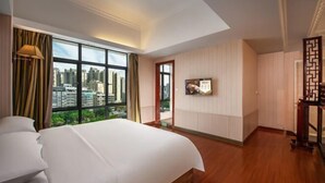 Habitación de hotel con una cama grande, un televisor montado en la pared y vistas a la ciudad a través de amplios ventanales.