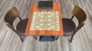A wooden table with a checkered board game, two chairs, and a black object on the table.