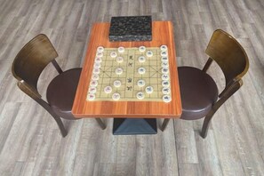 Een houten tafel met een schaakbordspel, twee stoelen en een zwart voorwerp op tafel.