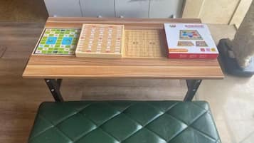 A wooden table with a green cushioned bench, a board game, and a book.