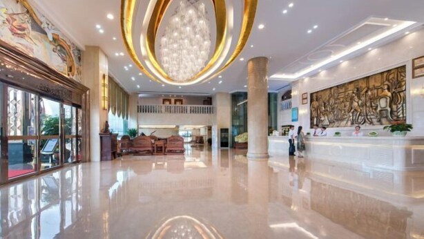 Un vestíbulo amplio con piso pulido, un candelabro imponente y una recepción con personal.