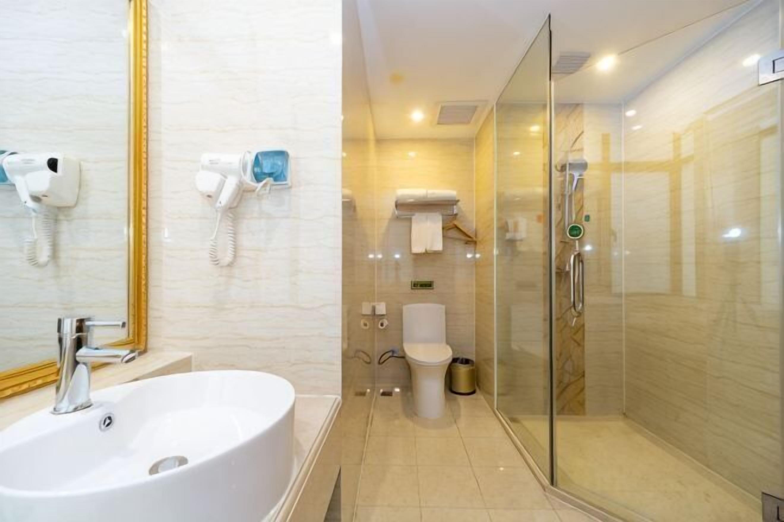 A bathroom with a large sink, a glass shower enclosure, a toilet, and a mirror with a gold frame.