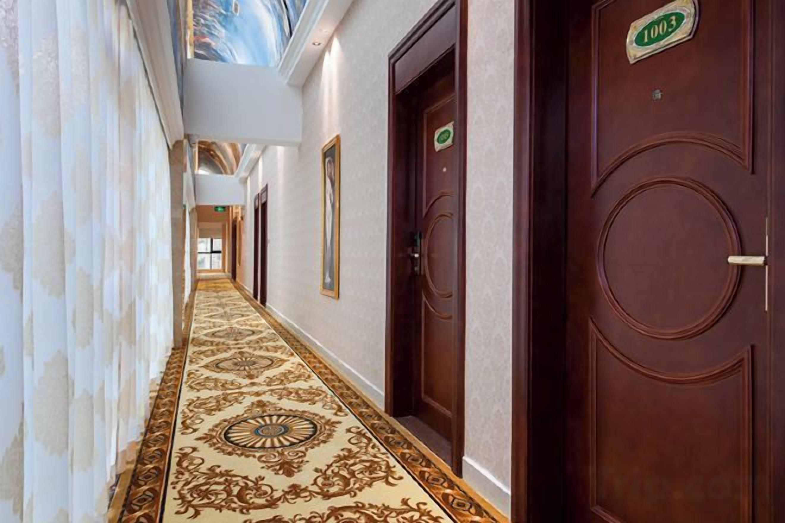 A hallway with ornate carpet, wooden doors, and a ceiling mural.