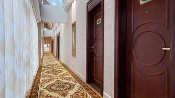 A hallway with ornate carpet, wooden doors, and a ceiling mural.
