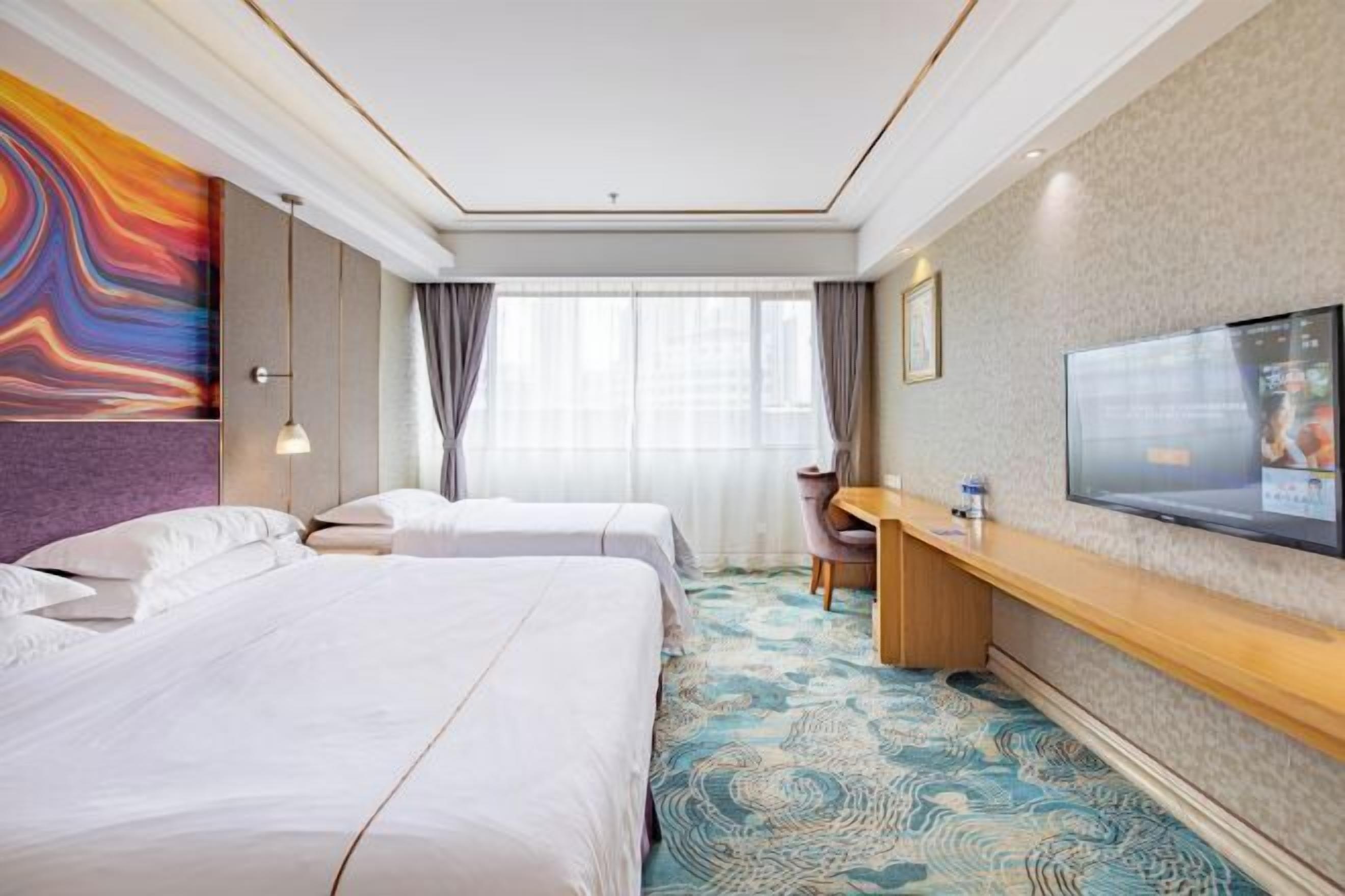 A hotel room with two beds, a desk, a TV, and a large window with curtains.