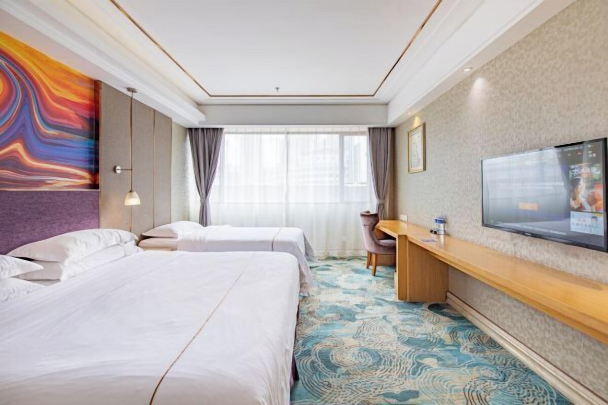 A hotel room with two beds, a desk, a TV, and a large window with curtains.