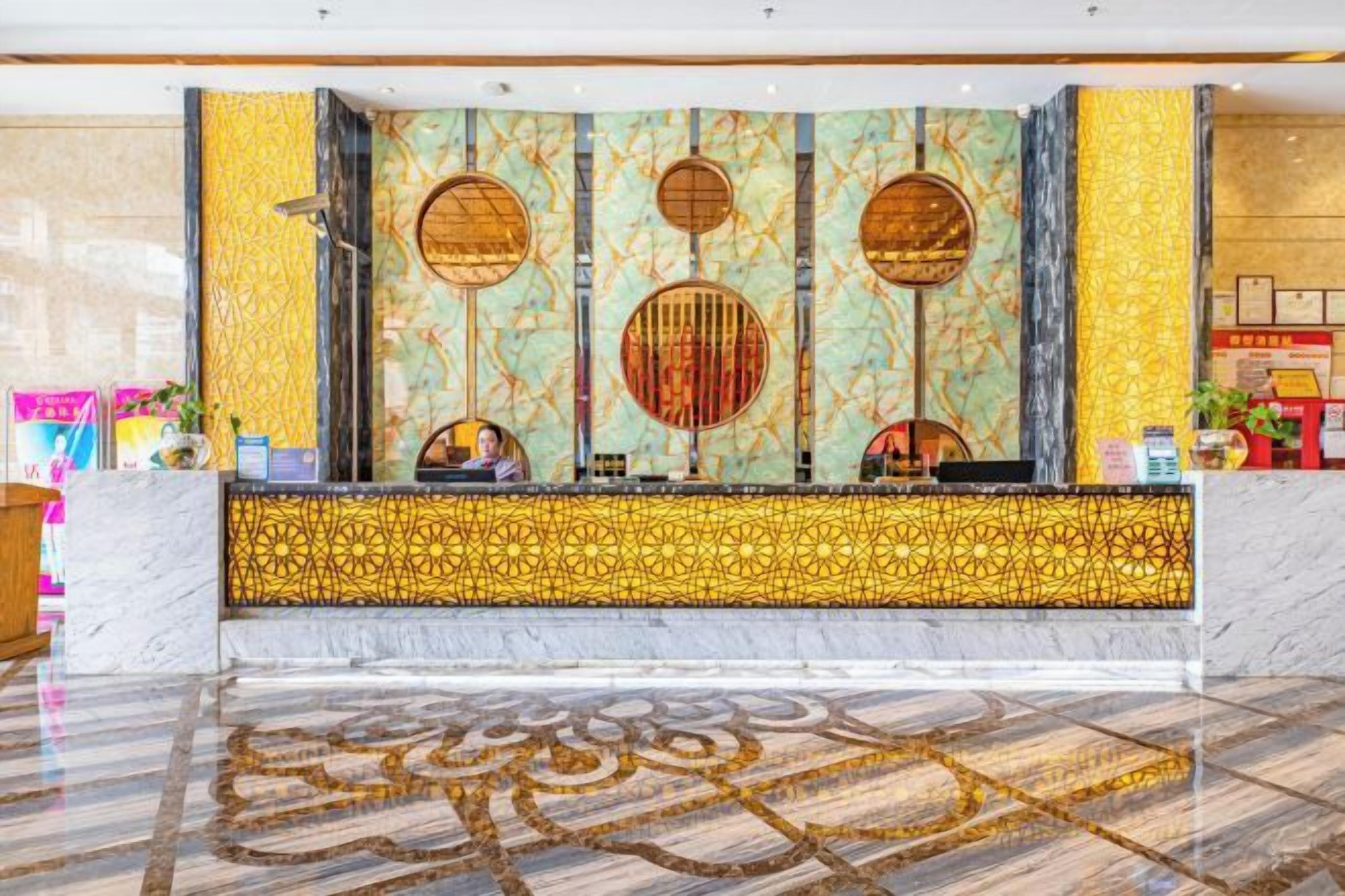 Un área de recepción con piso de mármol, una pared decorativa con diseños circulares y un mostrador de recepción.