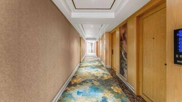 Un pasillo de hotel con alfombra estampada, puertas de madera y una pantalla digital en la pared.