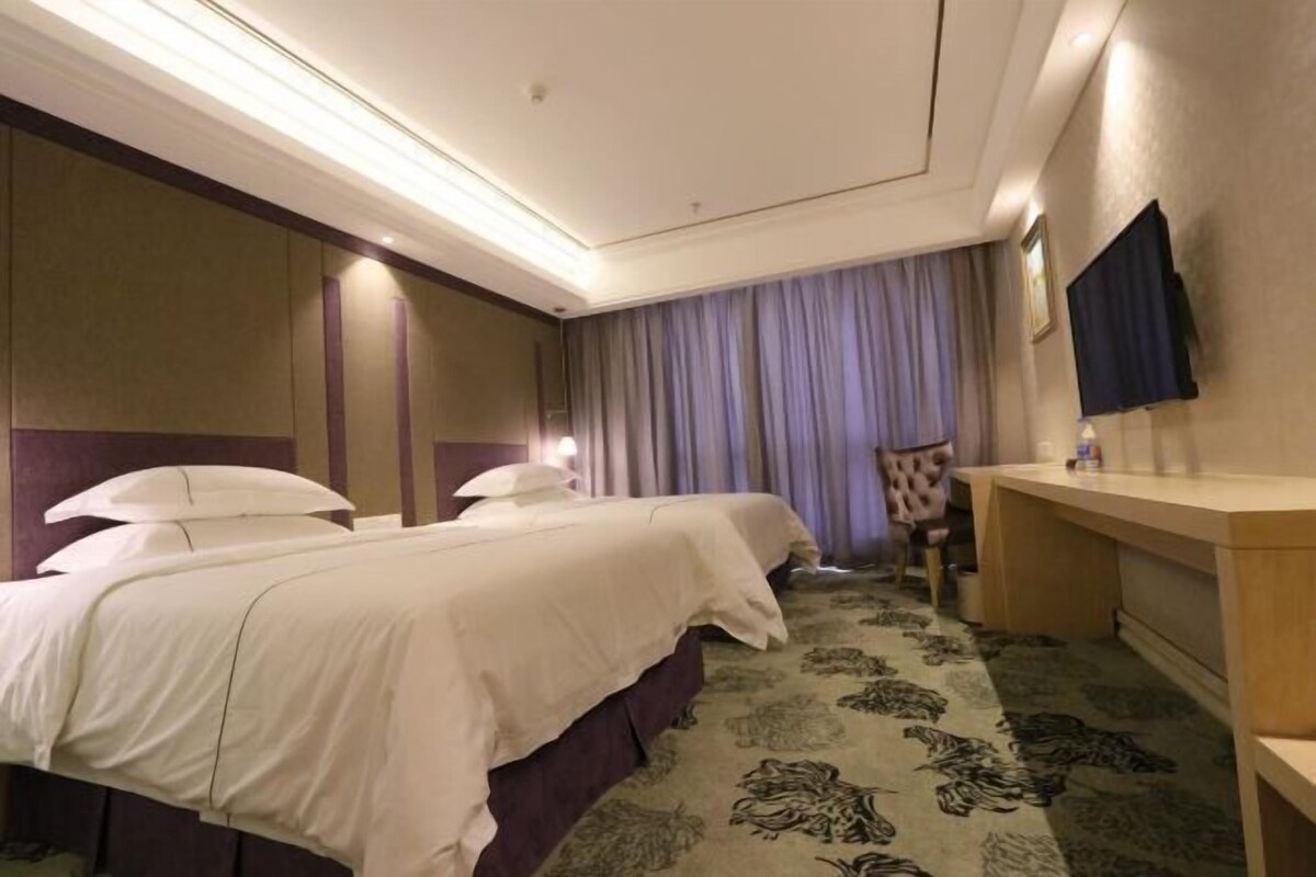 A hotel room with two beds, a desk, a chair, a TV, and a patterned carpet.