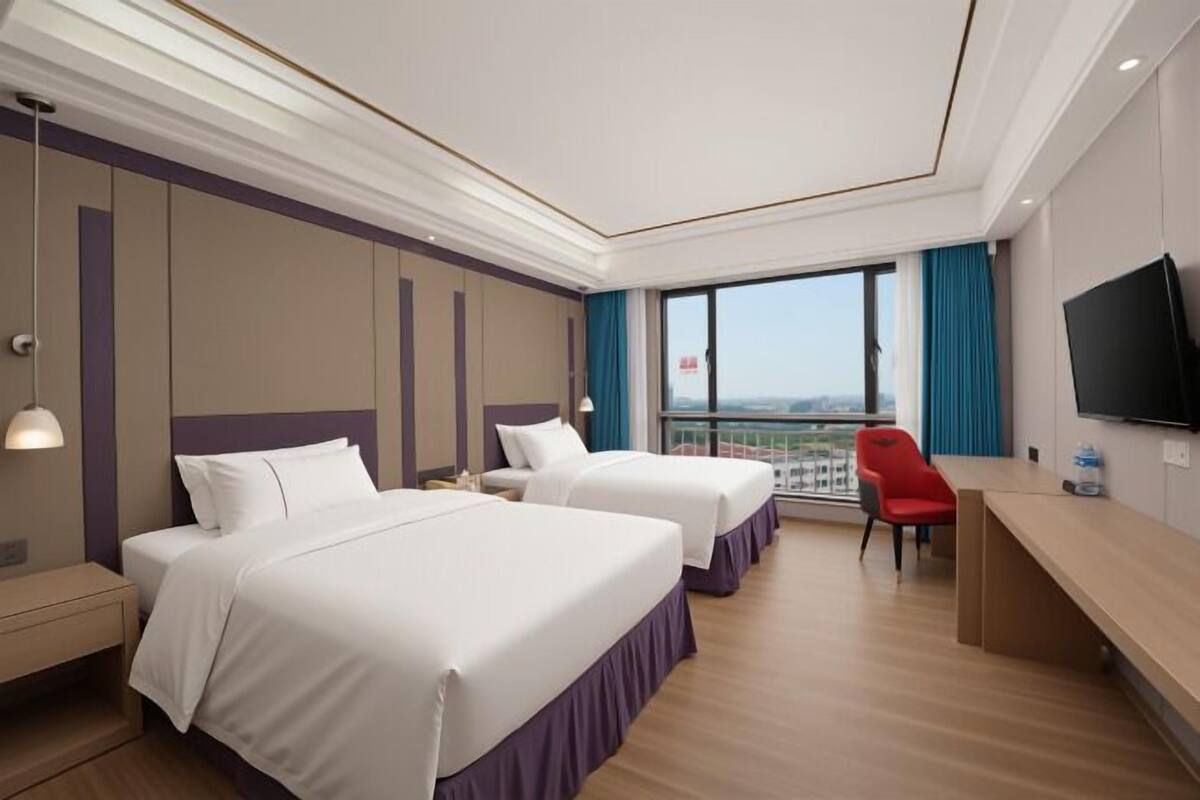 A hotel room with two beds, a desk, a chair, a TV, and a large window with a view.