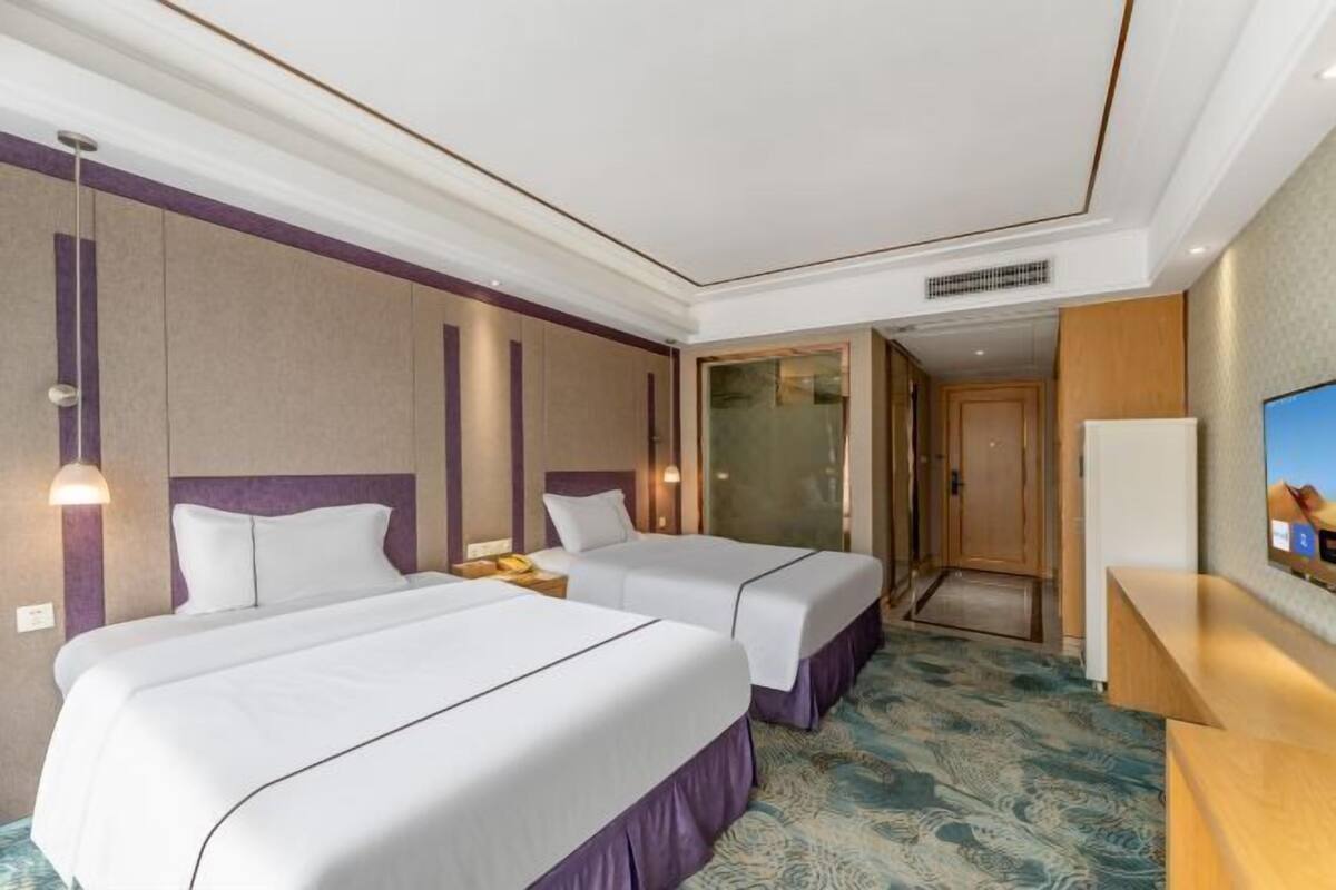 A hotel room with two beds, a television, and a bathroom visible through a glass door.