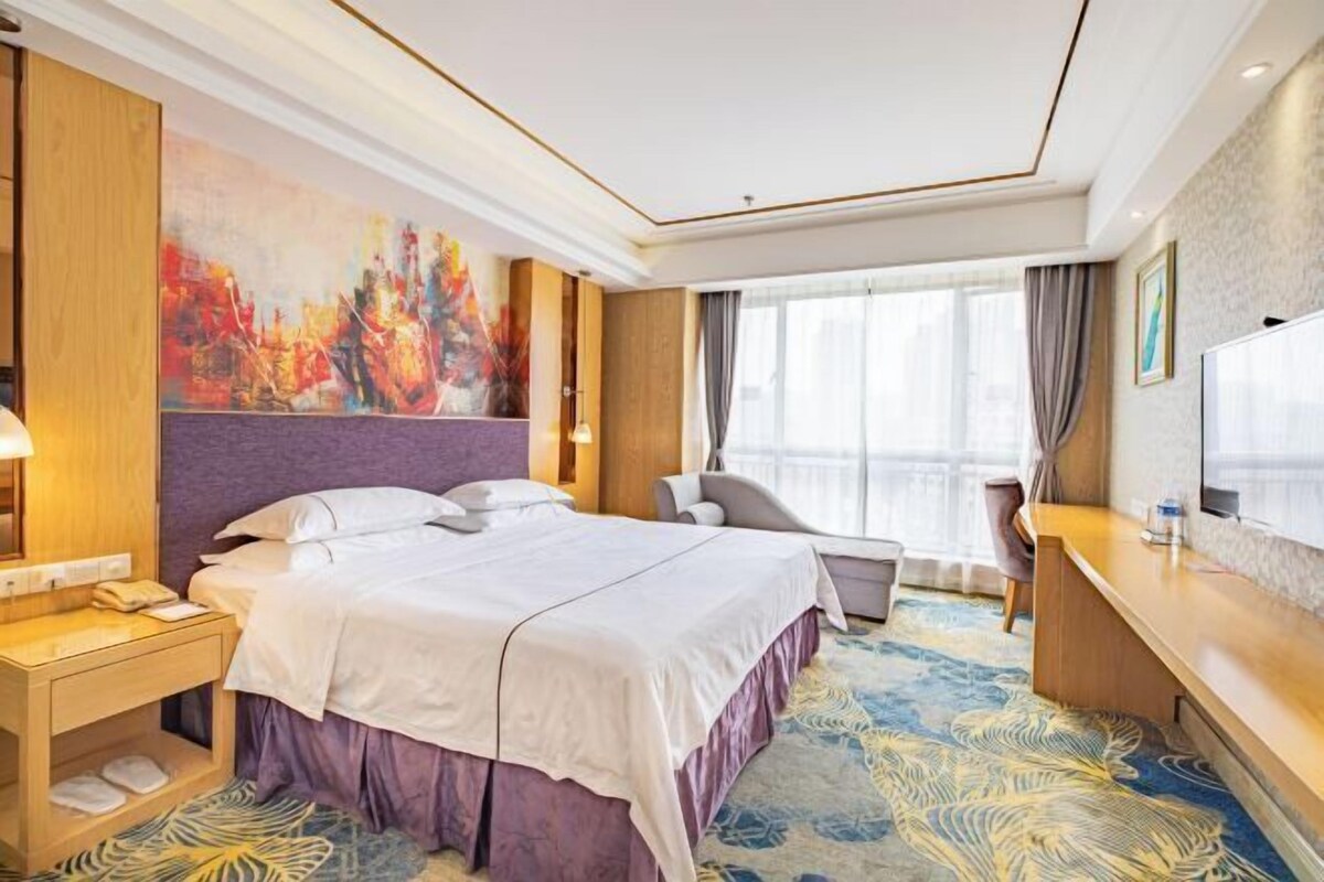 A hotel room with a large bed, a desk, a chair, and a TV.