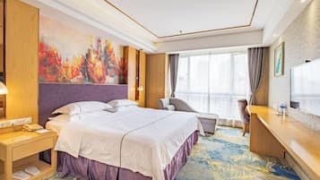A hotel room with a large bed, a desk, a chair, and a TV.