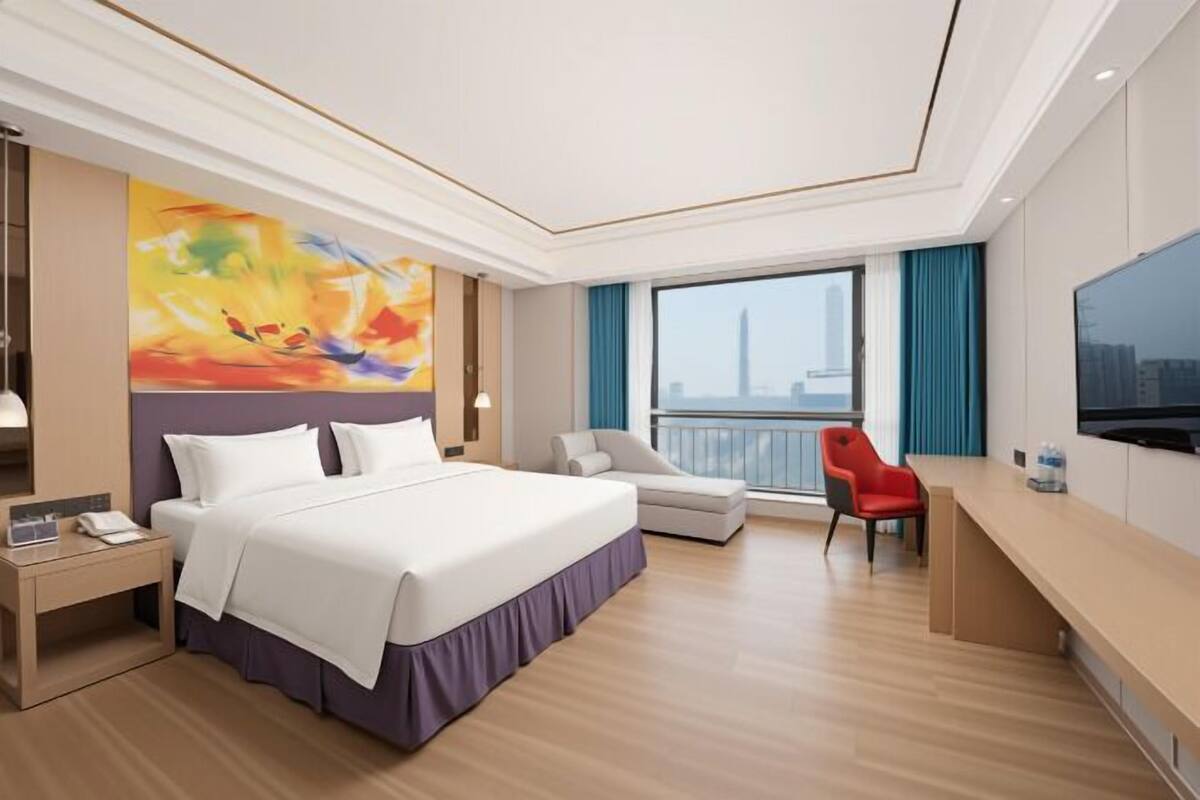 A hotel room with a bed, a desk, a chair, a TV, and a large window with a city view.