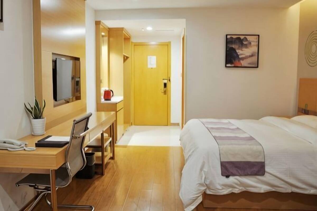 A hotel room with a bed, desk, chair, and a small table with a plant.