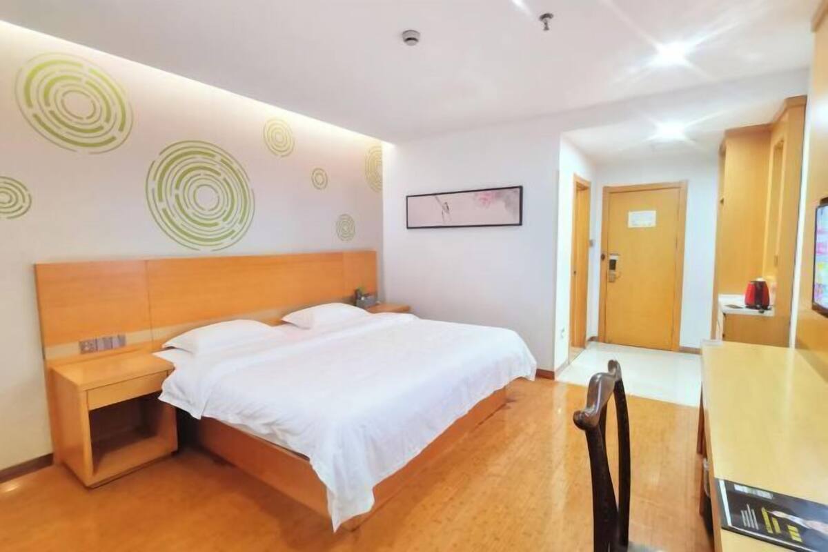 A hotel room with a bed, a nightstand, a wooden headboard, a wall with circular patterns, a framed picture, and a television on a stand.
