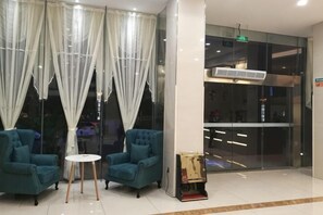 A lobby with two teal armchairs, a small round table, and a glass partition with a view. - GreenTree Inn (Yancheng Hongxing Meikailong Century Avenue) (Yancheng)