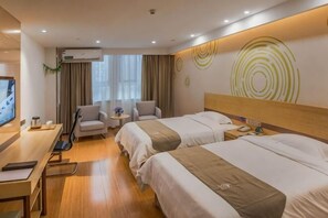 Quarto de hotel com duas camas, uma escrivaninha, uma televisão e uma mesinha de cabeceira com abajur.
