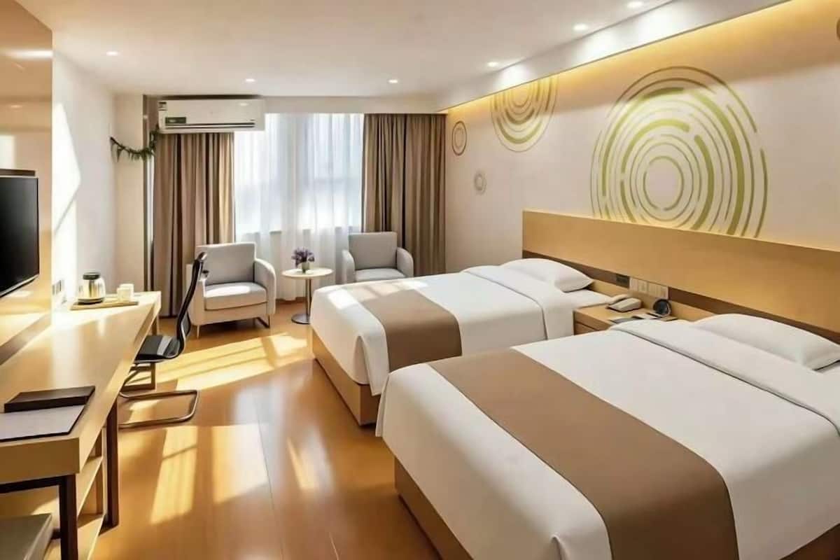 A hotel room with two beds, a desk, a chair, a TV, and a wall-mounted air conditioner.