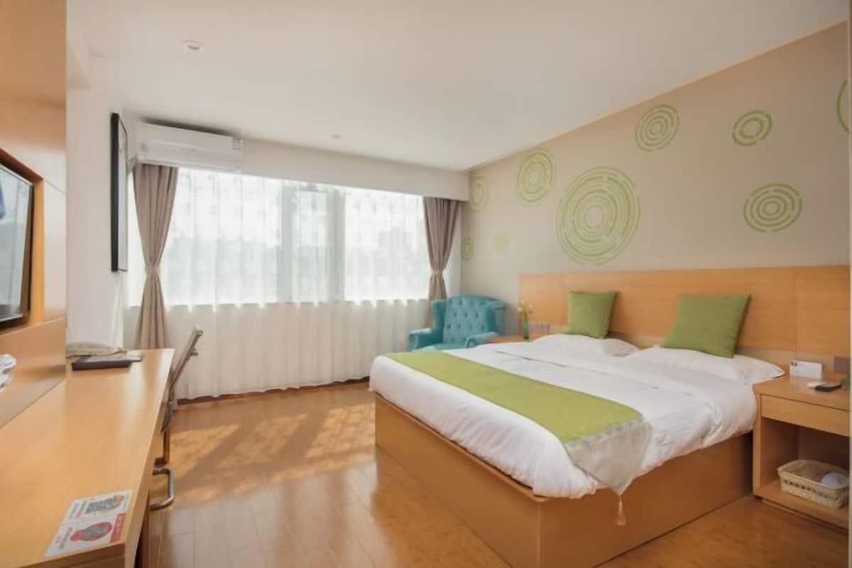 A hotel room with a bed, a desk, a chair, a TV, and a window with curtains.