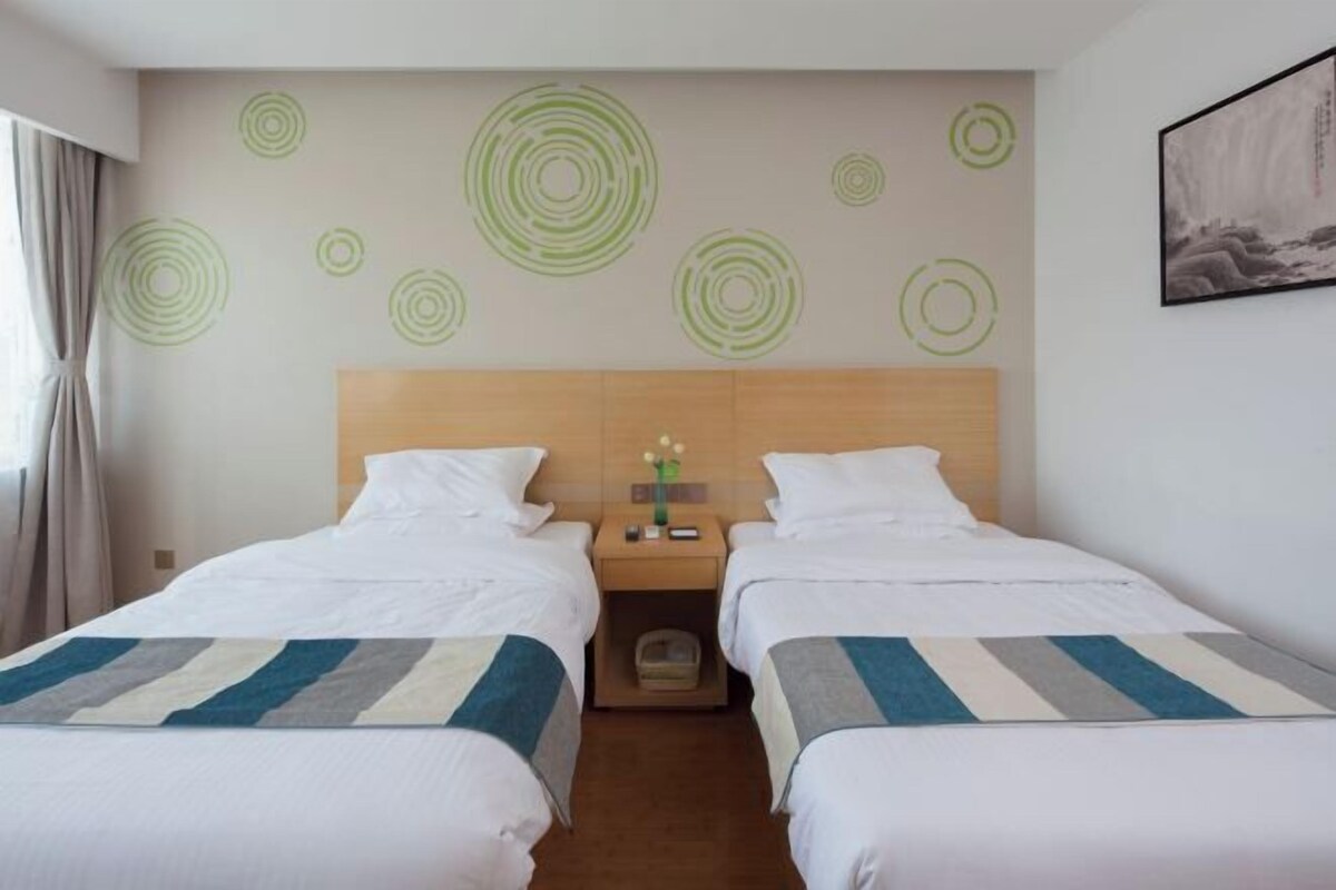 A hotel room with two beds, a wooden headboard, a nightstand with a vase, and a wall with circular patterns.