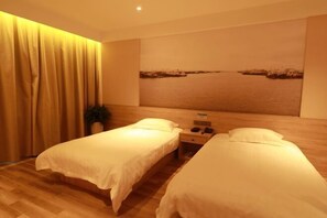 A hotel room with two single beds, a wooden floor, a large window with a view of the sea, and a painting of a beach scene.