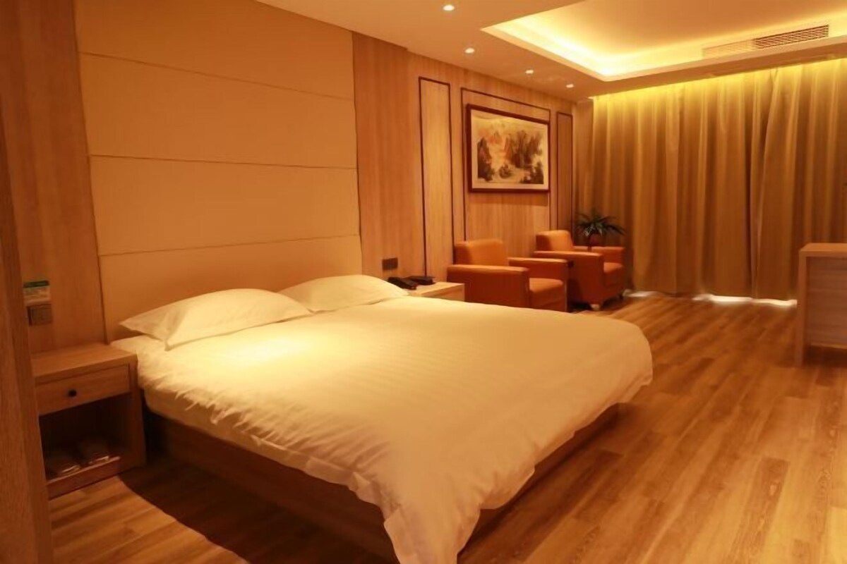 A hotel room with a large bed, wooden flooring, a nightstand, a chair, and a painting on the wall.