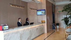 A modern reception desk with two staff members, a digital screen, and a marble counter.
