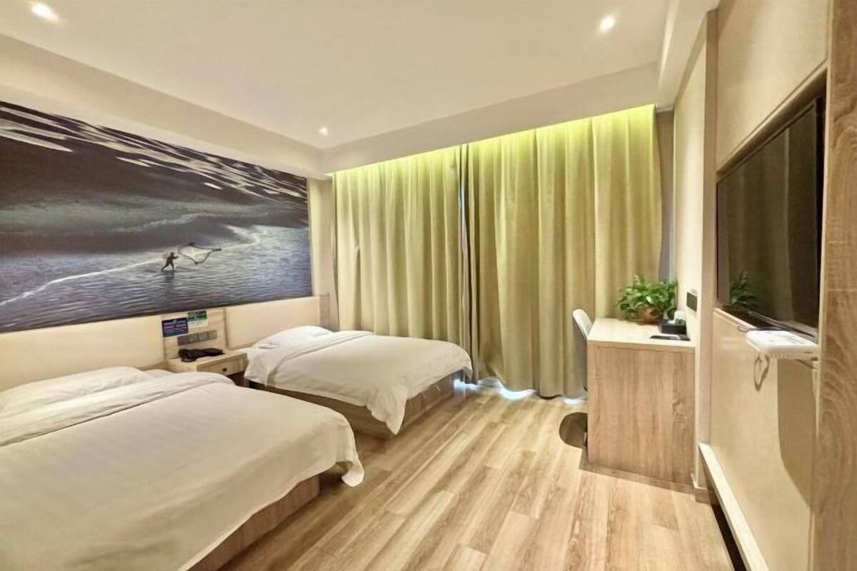 A hotel room with two beds, a large wall mural, a desk with a plant, and a TV.