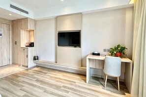 Een moderne kamer met een houten vloer, een bureau met stoel, een televisie en een potplant.