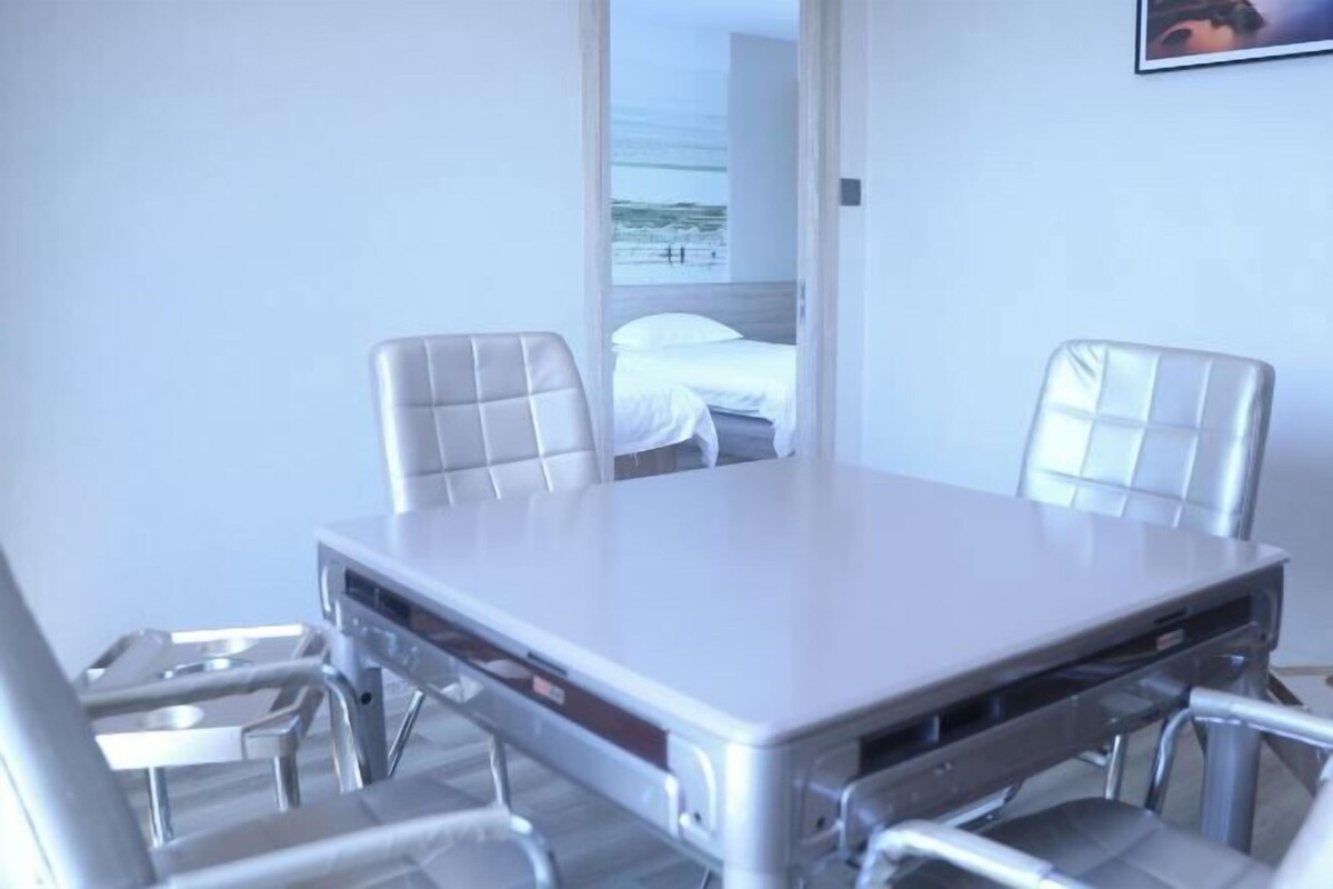 A modern hotel room with a large bed, a dining table with chairs, and a view of the beach through an open door.