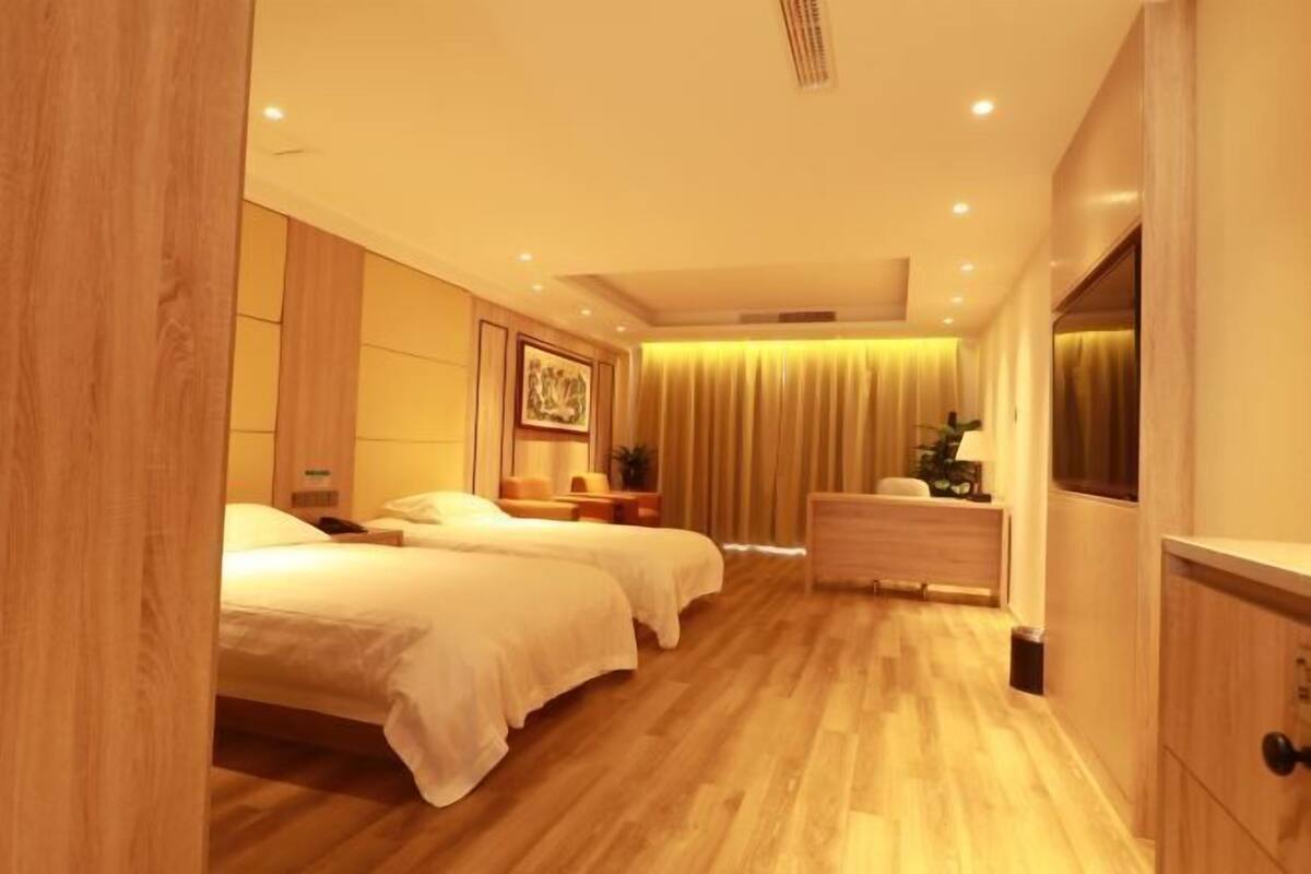 A modern hotel room with a wooden floor, two beds, a dresser, and a TV.