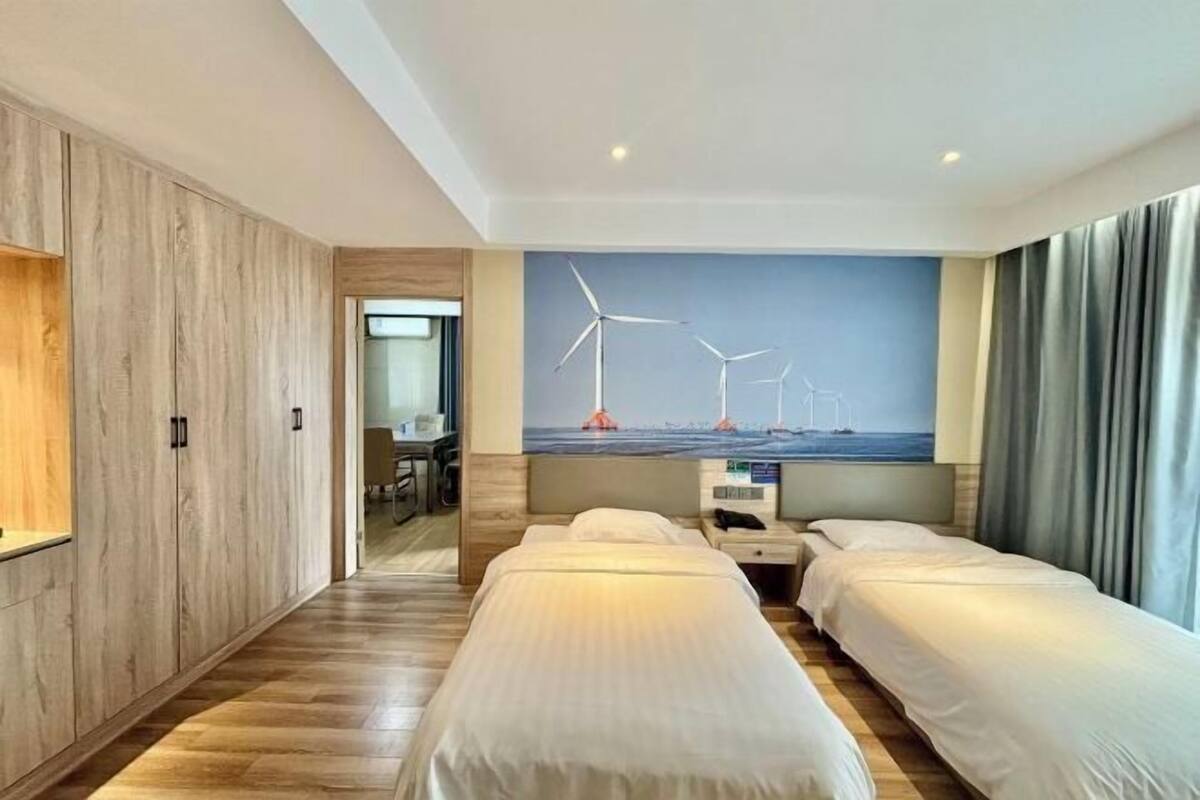 A hotel room with two beds, a desk, a chair, and a mural of wind turbines on the wall.