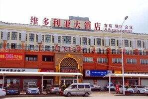 A hotel with multiple floors, a prominent entrance with a decorative arch, and several parked cars in front.