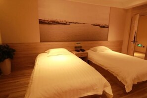 A hotel room with two single beds, a nightstand with a phone, and a painting of a lake on the wall.