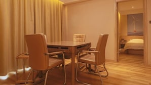A hotel room with a wooden dining table, four chairs, a bed, and a view of a wind turbine.