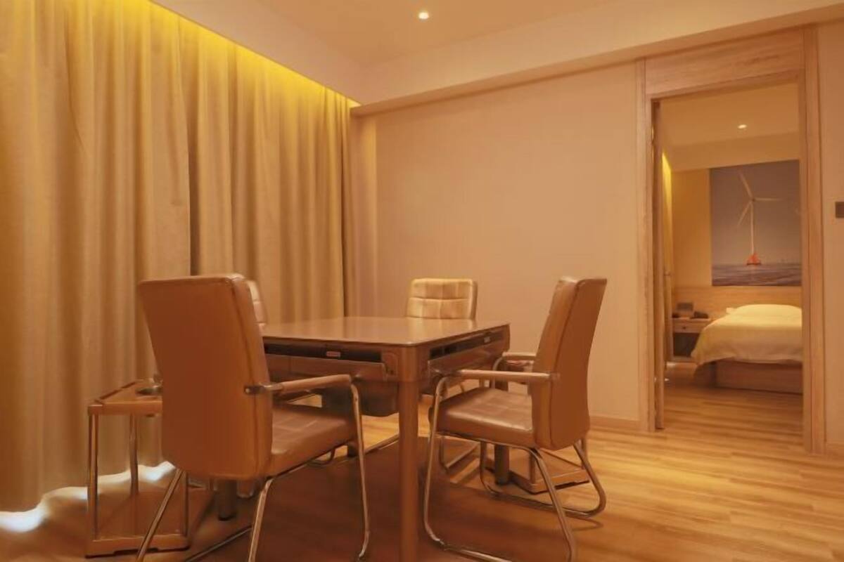A hotel room with a wooden dining table, four chairs, a bed, and a view of a wind turbine.
