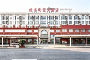 A hotel with a red and white facade, multiple windows, and a covered entrance area. - Rudong Victoria Hotel (Rudong)