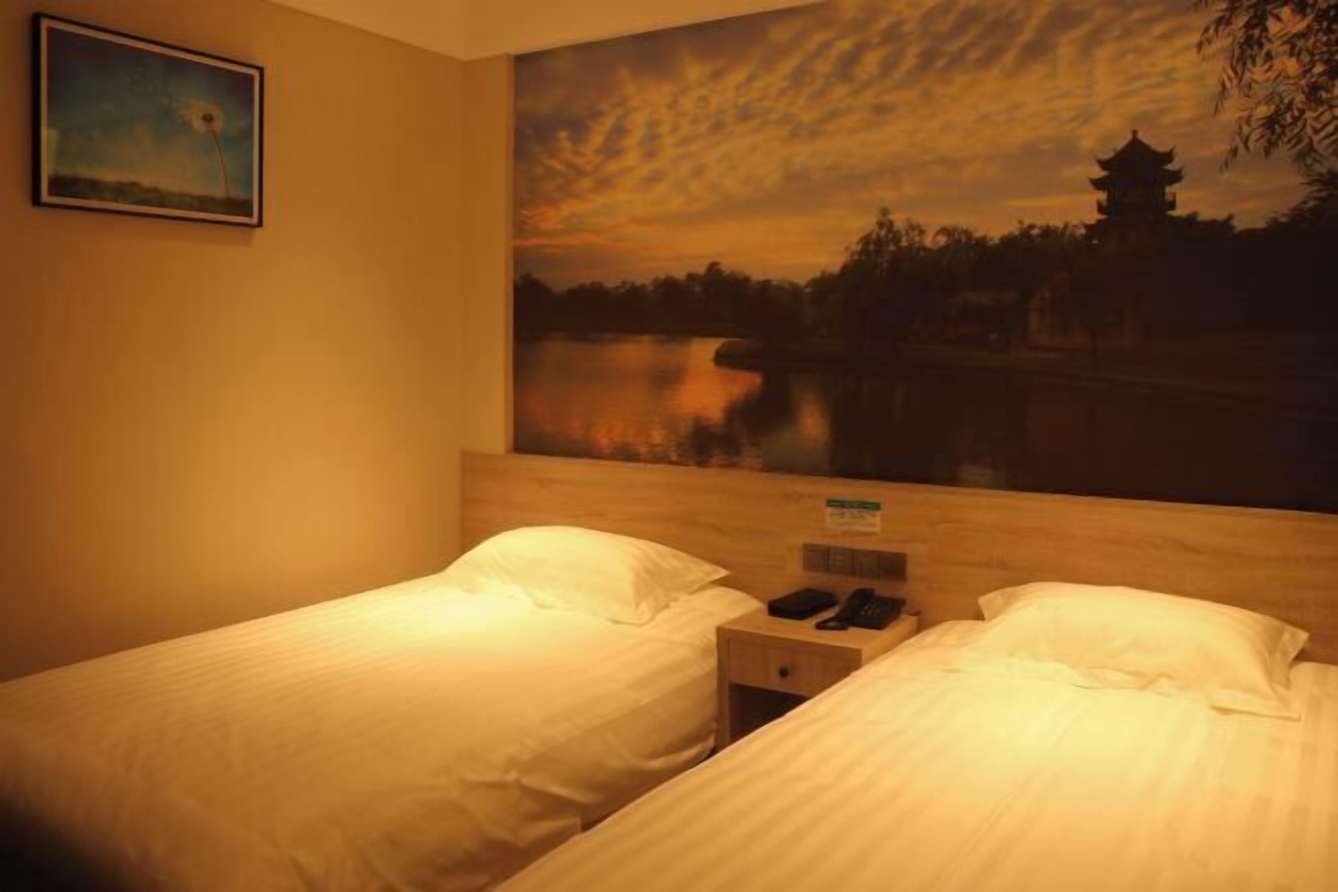 Quarto de hotel com duas camas, uma mesa de cabeceira com telefone e uma grande pintura de um pôr do sol sobre um lago com um pagode.