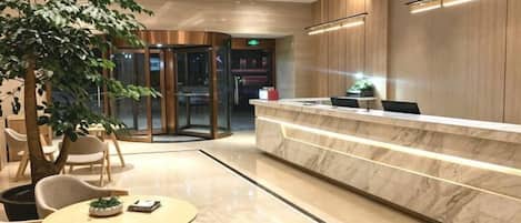 Un vestíbulo de hotel con mostrador de recepción, zona de estar y puerta giratoria.