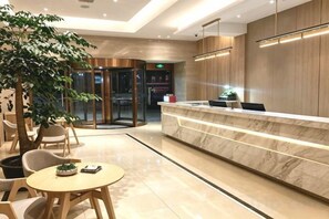 Um saguão de hotel com balcão de recepção, área de estar e porta giratória.