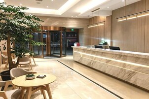 Un vestíbulo de hotel con mostrador de recepción, zona de estar y puerta giratoria.
