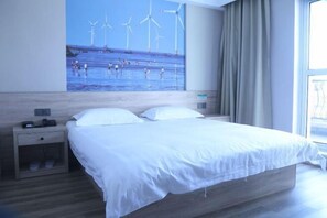 A hotel room with a large bed, a nightstand, a wall-mounted phone, and a window with curtains.