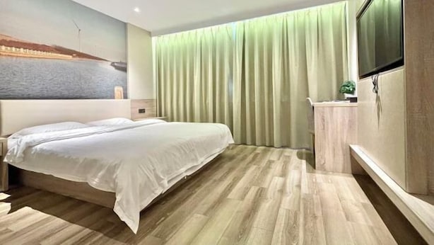 A hotel room with a bed, a TV, a curtain, and a painting on the wall.