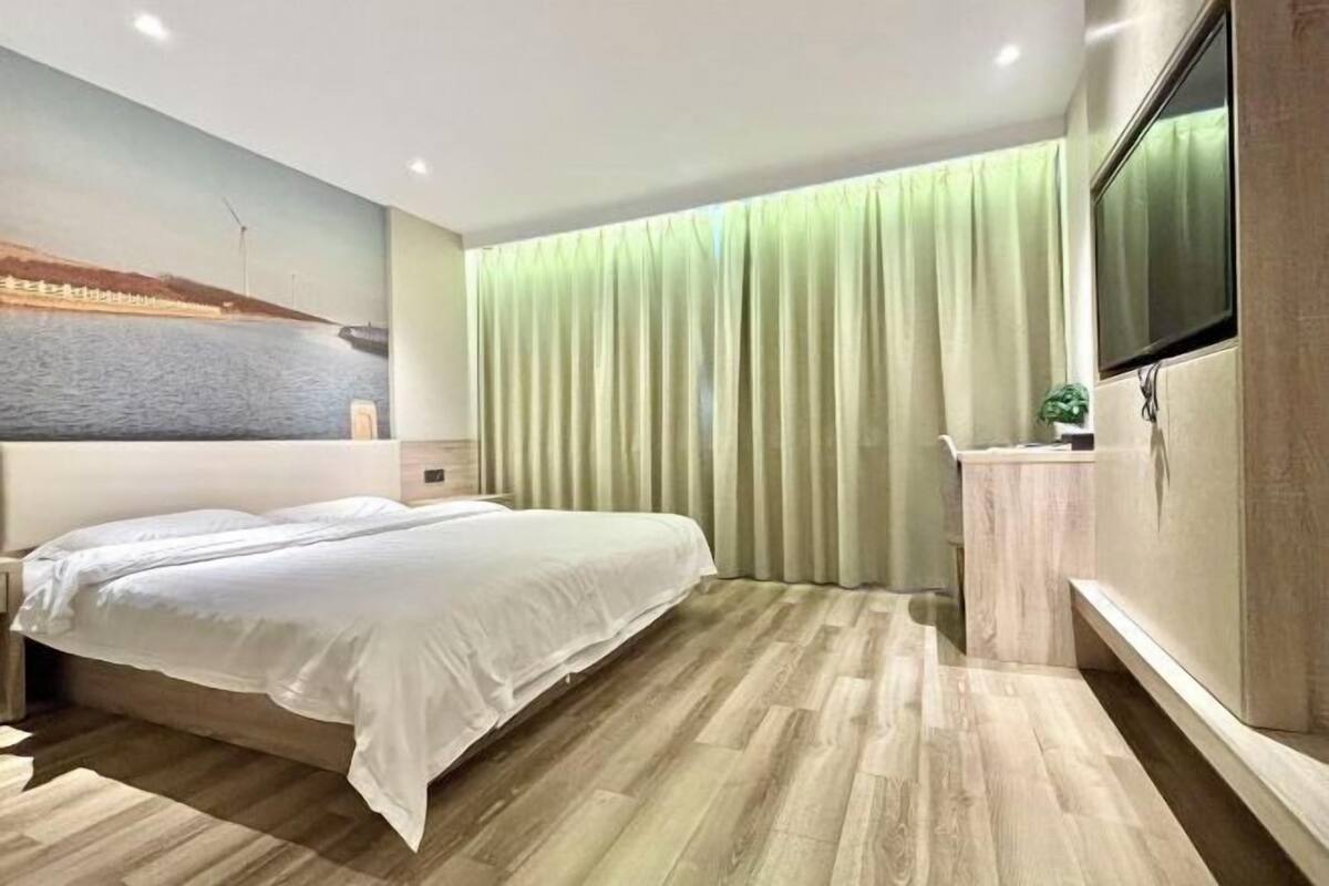 A hotel room with a bed, a TV, a curtain, and a painting on the wall.