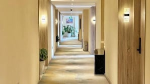 A hotel hallway with a marble floor, wooden doors, and potted plants.
