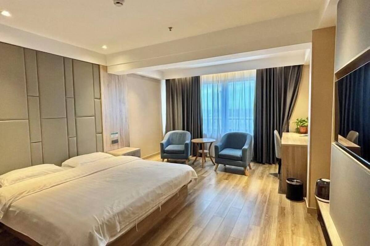A hotel room with a large bed, two armchairs, a small table, a desk, and a TV.
