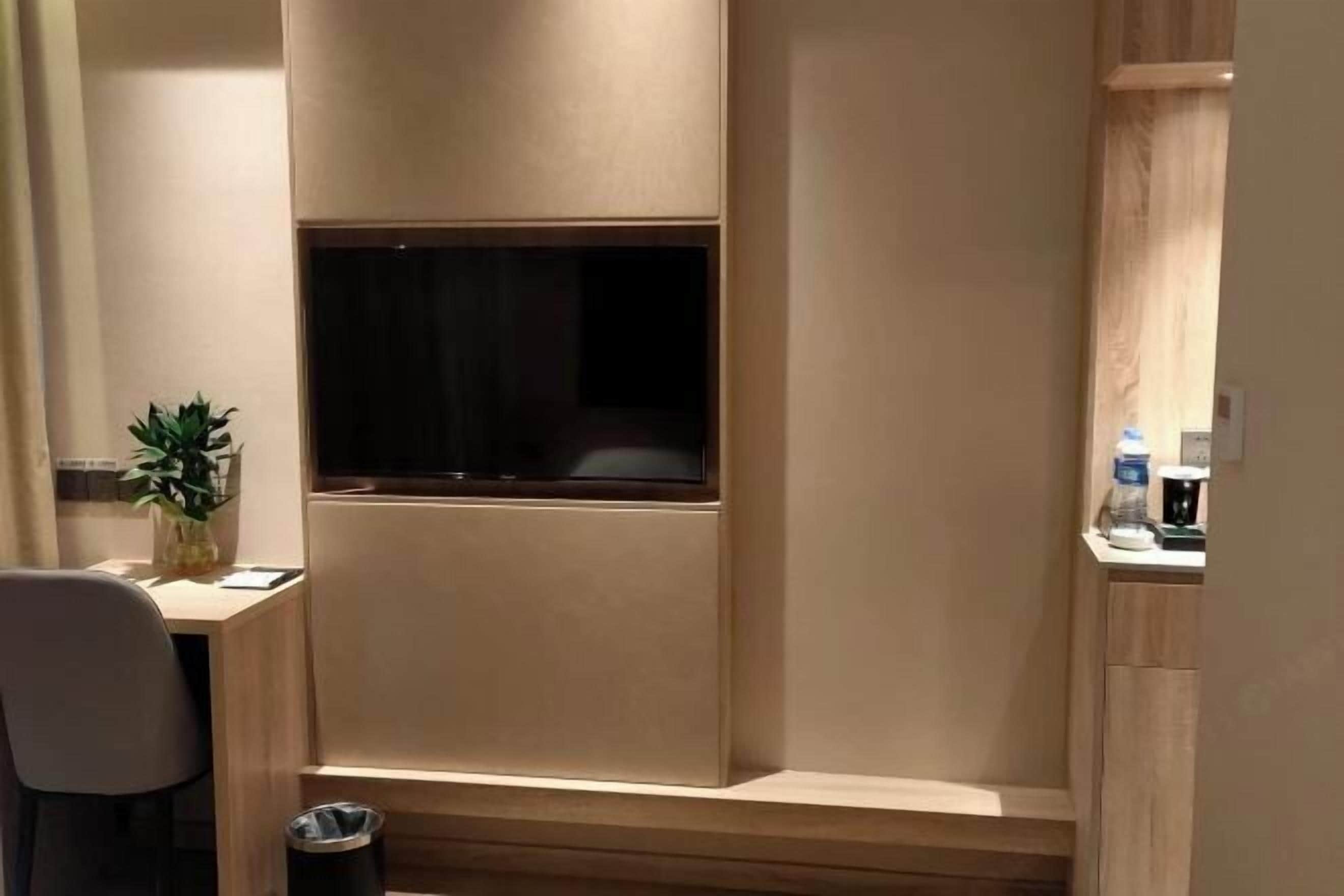 Una habitación moderna con televisión integrada, un escritorio pequeño, una silla y una planta en maceta.